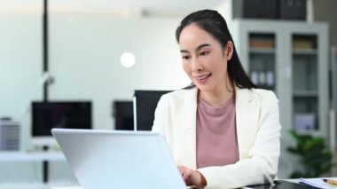 Modern ofiste dizüstü bilgisayarda çalışırken gülümseyen bir kadın