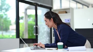 Masada otururken dizüstü bilgisayarda çalışan Asyalı iş kadını.