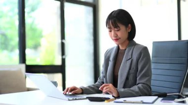 Gri ceketli genç Asyalı iş kadını modern ofiste çalışıyor.