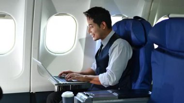 Genç işadamı uçak koltuğunda otururken dizüstü bilgisayarda çalışıyor.
