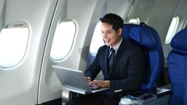 Asyalı işadamı uçak kabininde otururken dizüstü bilgisayarda çalışıyor.