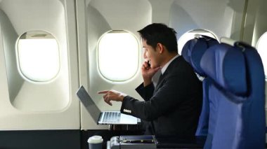 Genç işadamı uçak koltuğunda otururken dizüstü bilgisayarda çalışıyor.