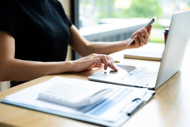 Modern bir çalışma alanında akıllı telefon ve dizüstü bilgisayar kullanan Asyalı iş kadını, dijital iletişim, verimlilik ve profesyonel uzaktan kumandayı sergiliyor..