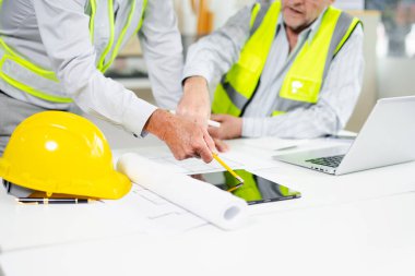 Çalışma ve tablet hakkında konuşan iki meslektaşım, ofisteki inşaat alanında mimari projeli dizüstü bilgisayar.