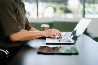 Modern ofis masasında dizüstü bilgisayarda kahve ve tabletle yazı yazan genç bir adam. Teknoloji, iş ve serbest meslek için ideal.