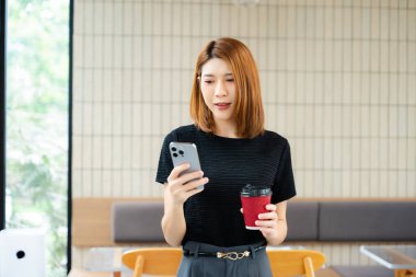 Asyalı iş kadını, dijital bağlantı, mobil verimlilik ve çağdaş mesleki yaşam tarzını vurgulayarak, modern bir ofis çalışma alanında akıllı telefonu dinliyor..