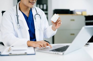 Doktor elinde ilaç şişesi tutarken dizüstü bilgisayarla çalışıyor. Dijital sağlık hizmetleri, reçete yönetimi ve teletıp hizmetleri kavramı.