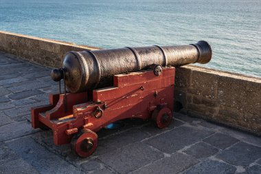 Saint-Malo, Brittany, Fransa 'nın taştan surları üzerinde sıcak akşam ışığı altında okyanus manzaralı kırmızı ahşap bir taşıt üzerinde eski demir top..