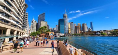 Sydney Harbour, Avustralya - 3 Nisan 2022: Modern şehir mimarisinin sergilendiği canlı bir liman sahnesi ve insanlarla dolu canlı bir gezinti alanı. 