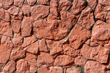 Close-up of a red stone wall with irregular rock pattern and visible mortar. Rough textured masonry surface suitable for backgrounds, construction, and architectural design.