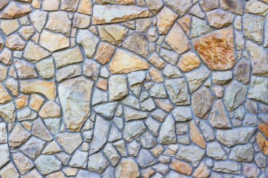 Texture of decorative stone wall made of irregularly shaped natural rocks in warm beige, yellow, gray tones. Rough surface and visible cement joints create rustic, handcrafted appearance, perfect for
