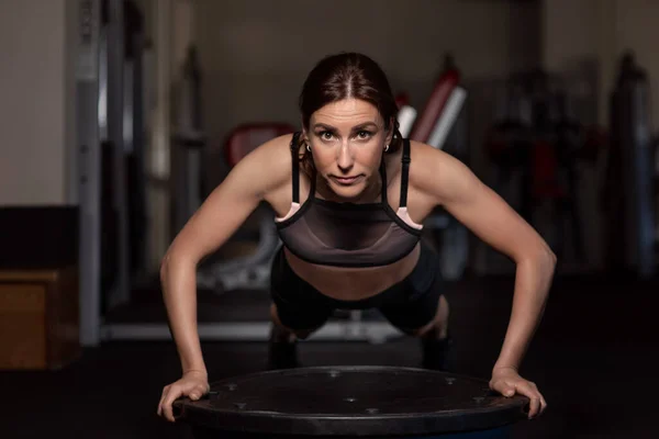 stock image Young woman doing push-ups in the gym on a balancing hemisphere.