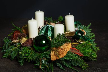 Dört beyaz Advent mumundan oluşan dekoratif çelenk, ladin dallarının koyu arkaplanında bir çelenk süslemesi. Gelenek Noel 'den önce gelir. Şenlikli natürmort.