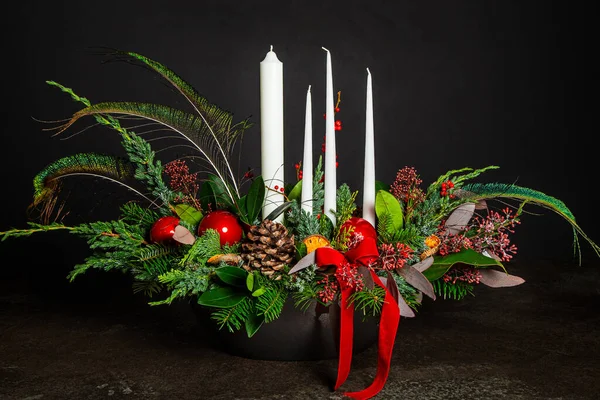 Symbolic Advent wreath with 4 candles Decorative wreath of four white Advent candles in an Advent wreath decoration with pine branches and peacock feathers on a dark background. Tradition before Christmas. Festive still life.