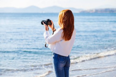 Kumsalda fotoğraf çeken genç bir kadın.