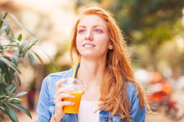 portrait of a beautiful young woman with orange juice in the park