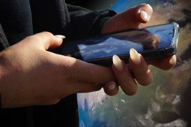 Hands of a girl with a smartphone on the background of planet Earth.