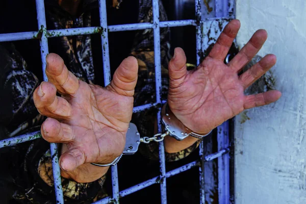 Hapishane parmaklıklarının arkasında elleri kelepçeli bir avuç içi. Bir yardım talebi.