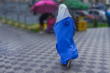 Mavi tesettürlü bir İslami kadın şehir caddesi boyunca yürüyor. Bulanık arkaplan.