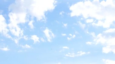 Kamera yukarı doğru hareket ediyor ve zengin mavi gökyüzüne dağılmış beyaz bulutları gösteriyor. Sakin hareket boşluk ve derinlik ekler..