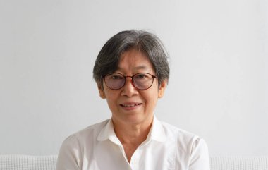 Yüzünde kırışıklık olan yaşlı bir kadının portresi, gözlük takıyor, gülümsüyor, mutlu bir şekilde bakıyor.