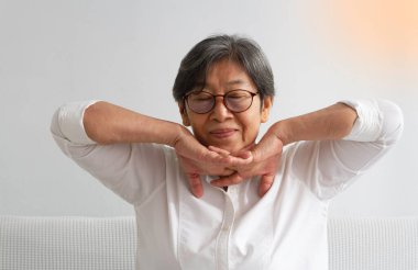Yüzünde kırışıklık olan yaşlı kadın, çene altından ellerini kavra ve yukarı kaldır, boyun etrafındaki kasları germek için, bulanık ışık