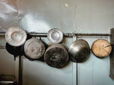 Duvarda asılı eski alüminyum mutfak gereçleri var. Tencere, tava ve ahşap kesme tahtaları var. Yerel pişirme aletleri..