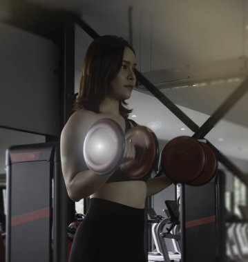 Formda ve sıkı vücutlu halterli genç bayan, spor salonunda egzersiz yapıyor, kas yapısı için, mercek alevi efekti, bulanık ışık..