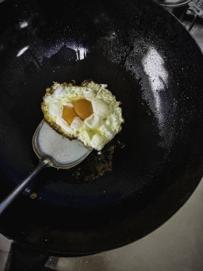 Paslanmaz spatula kepçesi siyah tavada güneşte kızartılmış yumurta, ev yapımı yemek..