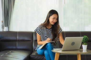 Coronaviruse ya da covid19 'dan korunmak için kanepeye dizüstü bilgisayar defteri ya da bilgisayar kullanan güzel Asyalı kadın portresi