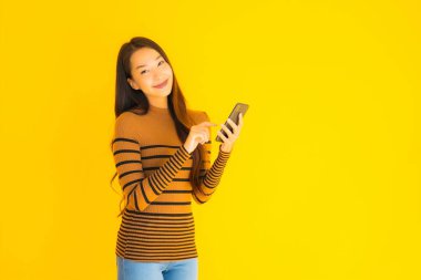 Güzel genç Asyalı kadın, sarı izole edilmiş arka planda birçok eylem içeren akıllı cep telefonu ya da cep telefonu kullanır.