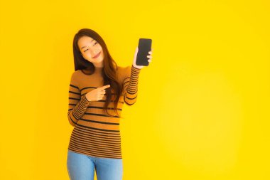 Güzel genç Asyalı kadın, sarı izole edilmiş arka planda birçok eylem içeren akıllı cep telefonu ya da cep telefonu kullanır.