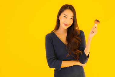 Sarı izole arkaplanda makyaj fırçası olan güzel bir Asyalı kadın portresi.