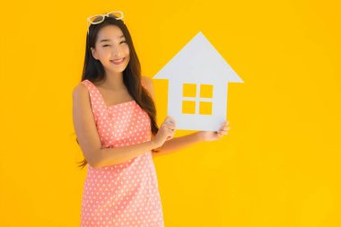 Güzel genç Asyalı kadın sarı izole arka planda ev ya da ev tabelasını gösteriyor.