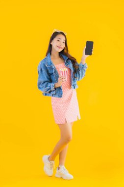 Güzel bir Asyalı kadın portresi telefon patlamış mısırı ve sarı izole edilmiş bir arka planda film izlemekten memnun.
