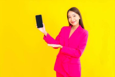 Güzel bir Asyalı kadın portresi sarı renkli izole edilmiş arka planda akıllı cep telefonu kullanır.