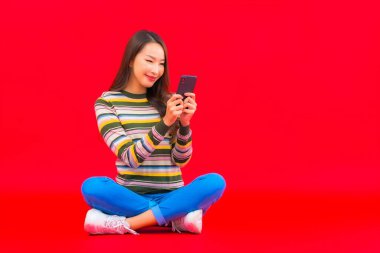 Güzel bir Asyalı kadın portresi kırmızı izole edilmiş arka planda akıllı cep telefonu kullanıyor.