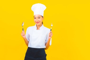 Güzel bir portre genç Asyalı kadın aşçı ya da aşçı üniforması giyiyor sarı izole arka planda çatal ve kaşıkla.