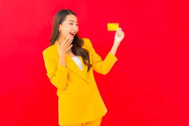 Güzel bir Asyalı kadının portresi kırmızı arka planda kredi kartıyla cep telefonu kullanıyor.