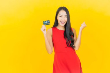 Asyalı güzel bir kadının portresi. Sarı arka planda kredi kartıyla gülümsüyor.