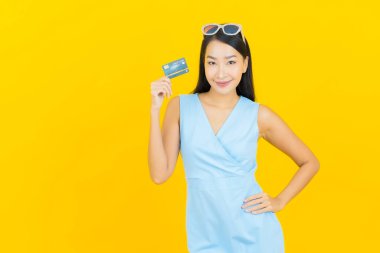 Asyalı güzel bir kadının portresi. Sarı arka planda kredi kartıyla gülümsüyor.