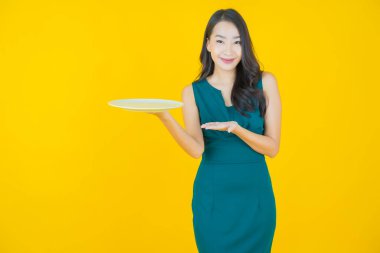 Güzel Asyalı bir kadının portresi. Arka planda boş tabak tabağıyla gülümsüyor.