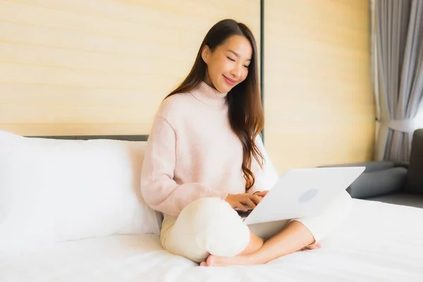在卧室内用手提电脑和手机描绘美丽的年轻亚洲女人 — 图库照片
