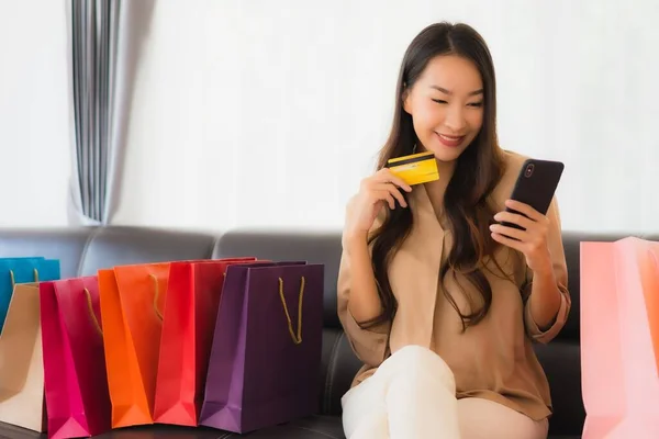 신용카드와 스마트폰으로 온라인 쇼핑을 아름다운 아시아 여성의 거실에 쇼핑백을 봅니다 — 스톡 사진