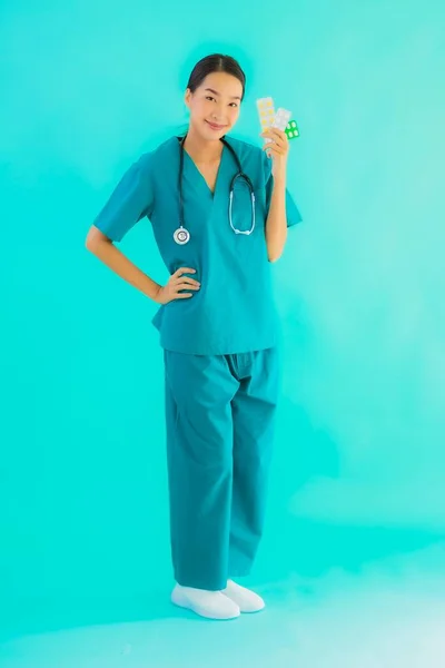 肖像画美しいです若いですアジアの医師女性とともに丸薬や薬上の青隔離された背景 — ストック写真