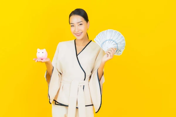 肖像画美しい若いビジネスアジアの女性とともに多くの現金お金と貯金箱上の黄色の背景 — ストック写真