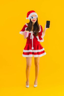 Güzel bir Asyalı kadın portresi patlamış mısır ve 3D gözlüklü noel şapkası takıyor sarı izole edilmiş arka planda film izlemeye hazır.