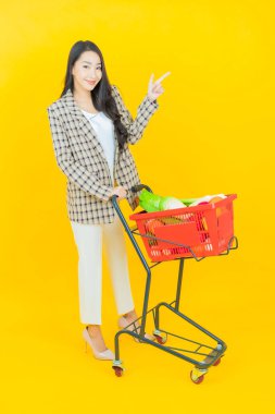 Renkli arka planda süpermarketten alınmış market sepetiyle gülümseyen güzel Asyalı kadın portresi.