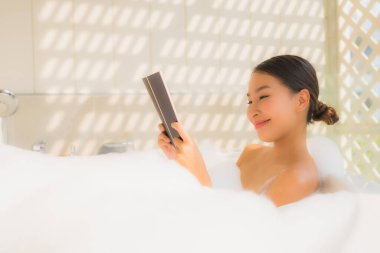 Genç Asyalı kadın spa konsepti için küvette kitap okudu.