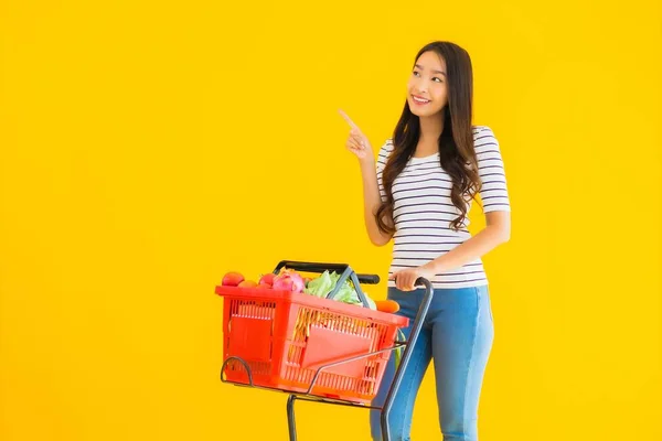 ポートレート美しい若いアジアの女性スーパーマーケットから食料品を買い物し 黄色の隔離された背景にカート — ストック写真